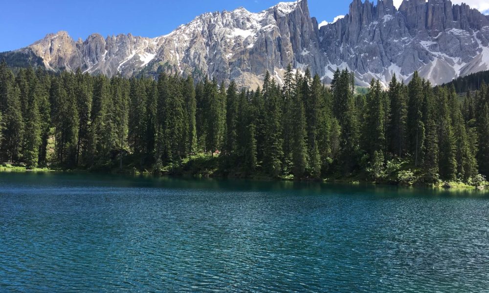 Lago di Carezza con acqua blu-verde, bosco e montagne sullo sfondo