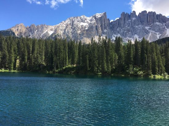 Lago di Carezza con acqua blu-verde, bosco e montagne sullo sfondo