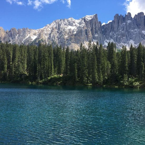 Lago di Carezza con acqua blu-verde, bosco e montagne sullo sfondo