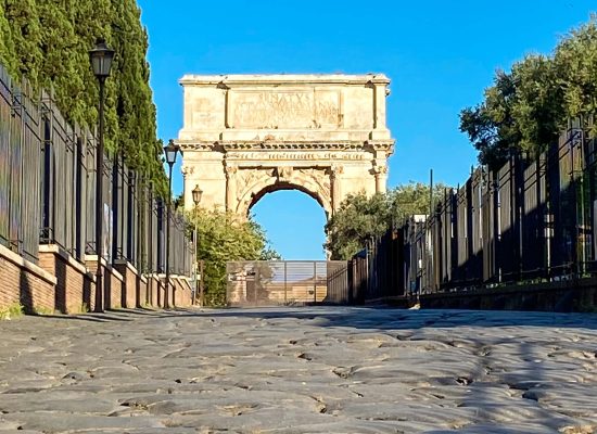 Antica pavimentazione della Via Sacra a Roma con l’Arco di Tito sullo sfondo, visti da una prospettiva rasoterra.