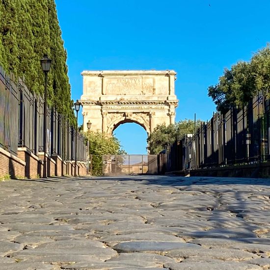 Antica pavimentazione della Via Sacra a Roma con l’Arco di Tito sullo sfondo, visti da una prospettiva rasoterra.