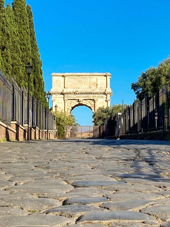 Antica pavimentazione della Via Sacra a Roma con l’Arco di Tito sullo sfondo, visti da una prospettiva rasoterra.