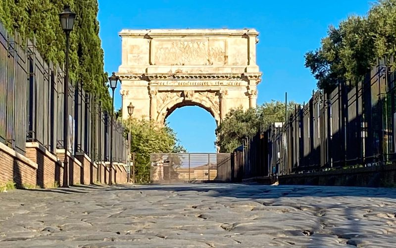 Antica pavimentazione della Via Sacra a Roma con l’Arco di Tito sullo sfondo, visti da una prospettiva rasoterra.